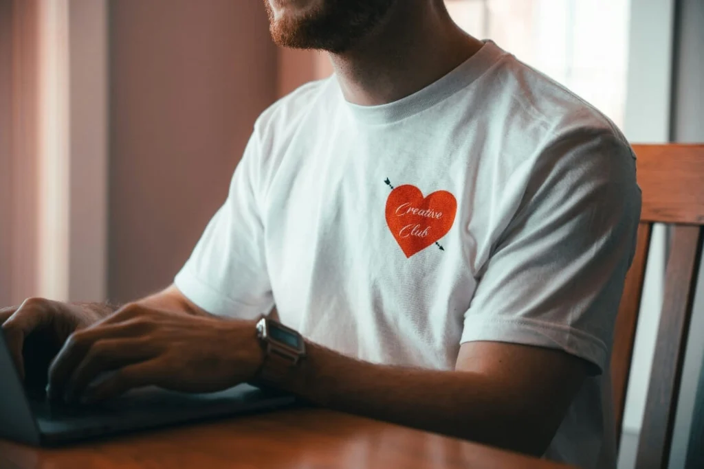 Person in a white T-shirt typing on a laptop